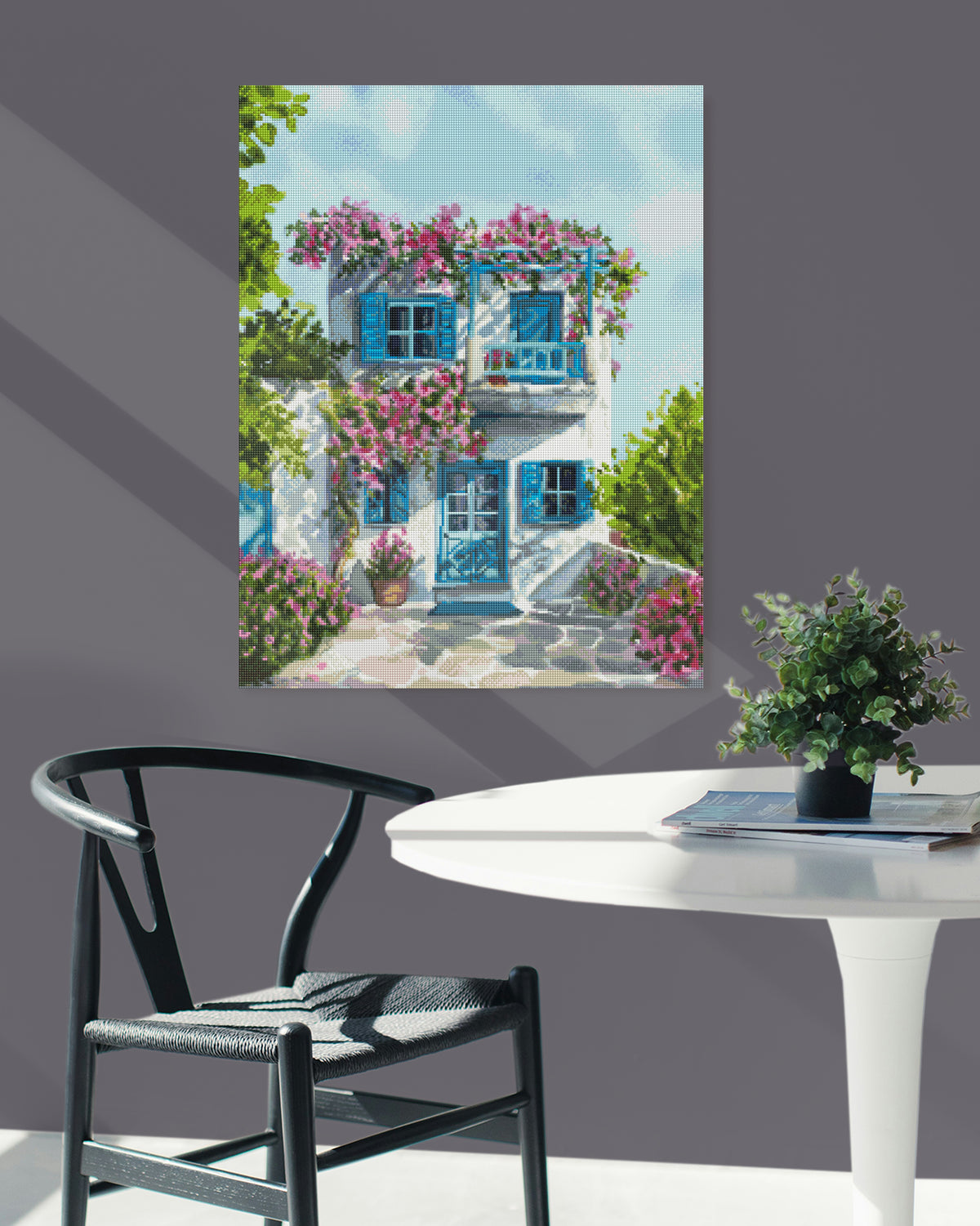 Idyllisches Diamond Painting mit weißem Haus, blau-türkisen Fensterläden und Türen und rosafarbenen Blüten als dekorative Wanddekoration